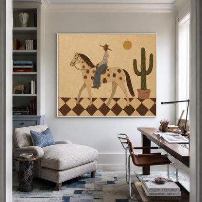 May include: A framed wall art print featuring a stylized illustration of a person in a hat riding a spotted horse across a brown and white checkered floor. A tall green cactus in a pot and a yellow sun are visible against a tan background.