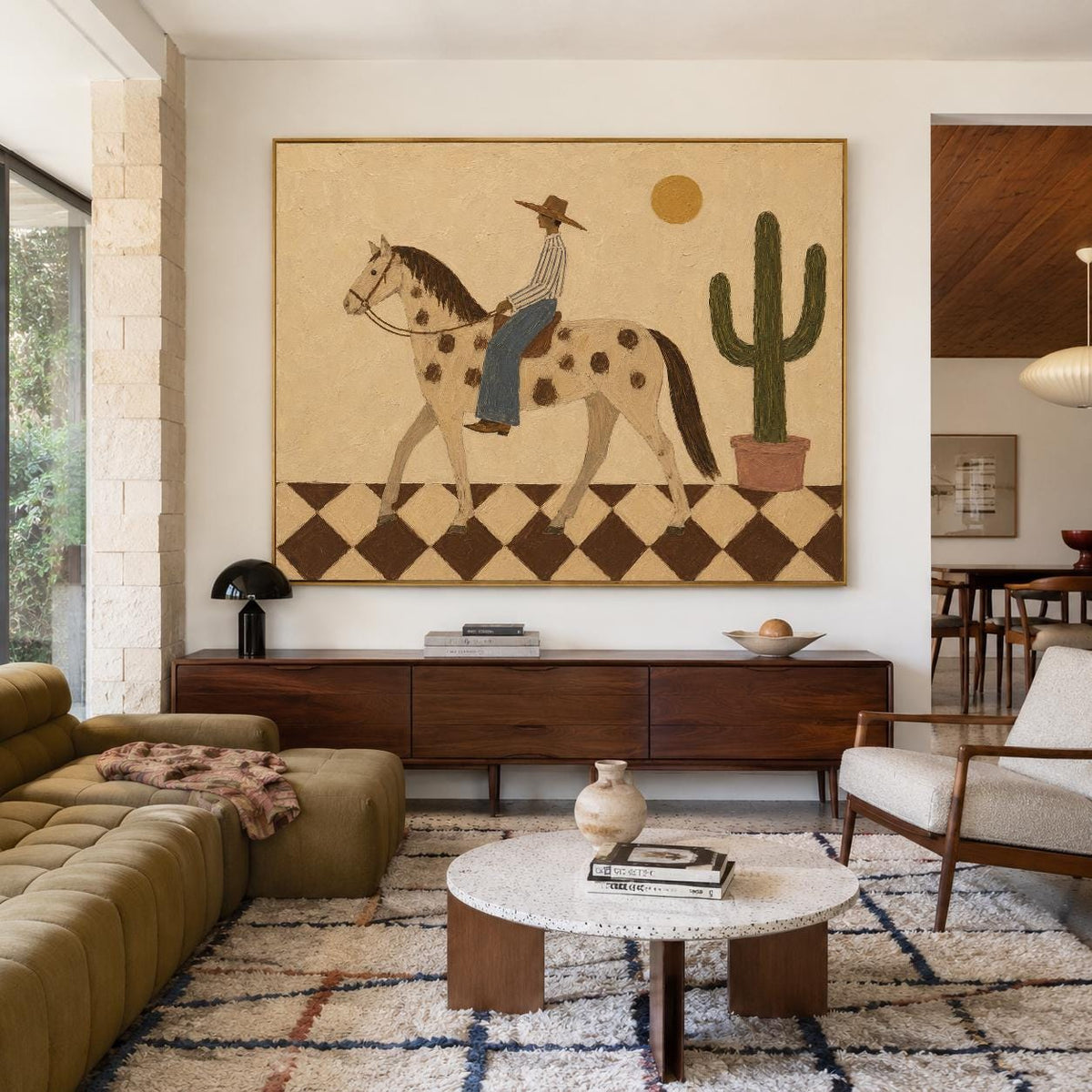 May include: A large rectangular wall art piece featuring a stylized illustration of a person in a hat riding a spotted horse across a brown and cream checkered floor, with a tall green cactus in a pot and a yellow sun against a beige background.