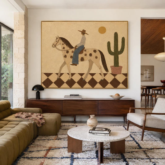 May include: A large rectangular wall art piece featuring a stylized illustration of a person in a hat riding a spotted horse across a brown and cream checkered floor, with a tall green cactus in a pot and a yellow sun against a beige background.