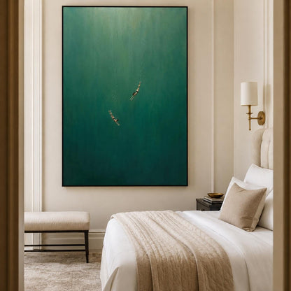 May include: A large rectangular wall art piece featuring a deep emerald green gradient background with two small figures swimming downward in the center. The painting is framed in a thin black border and hangs on a neutral beige wall above a bed.