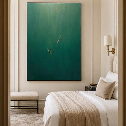 May include: A large rectangular wall art piece featuring a deep emerald green gradient background with two small figures swimming downward in the center. The painting is framed in a thin black border and hangs on a neutral beige wall above a bed.