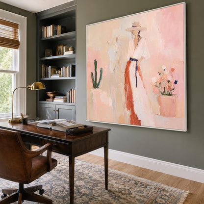 May include: A large square framed painting hanging on a wall, depicting a figure wearing a wide-brimmed hat and a long white dress with a red accent, standing beside a white horse, a green cactus, and a potted plant with colorful flowers.